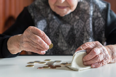 Elderly woman sitting at the table counting money in her wallet - em360