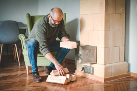 Mature adult man lights up the fireplace - em360